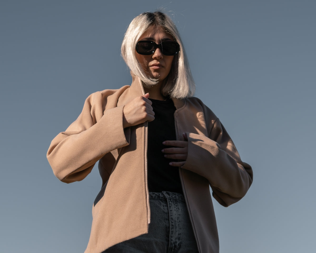 a woman with white hair wearing a tan jacket and sunglasses