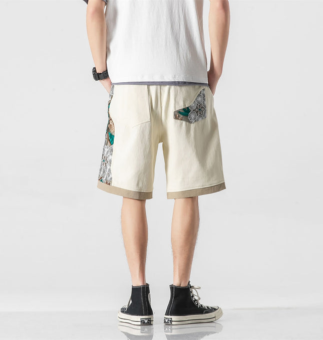 Rear view of a man wearing trendy men's street style embroidered work shorts in relaxed, organic cotton fabric, with a white t-shirt and black sneakers.