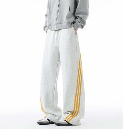 Heavyweight Three-Stripe Pants - Loose Fit displayed in a sporty gray outfit with yellow stripes.