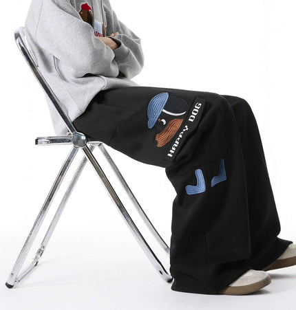 Dog Embroidered Sweatpants - Loose Fit worn by a person sitting on a chair, showcasing playful dog embroidery.