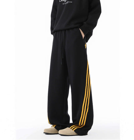 Heavyweight Three-Stripe Pants - Loose Fit with sporty design, elastic polyester fabric, and bold yellow stripe detailing.