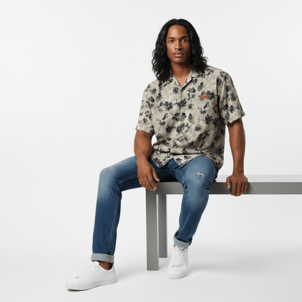 Floral Print Short Sleeve Shirt – Loose Fit worn by a model sitting on a bench, showcasing casual summer style.