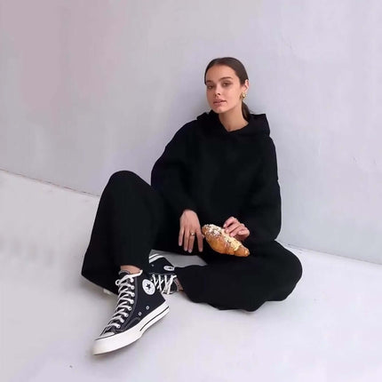 Cotton Blend Two-Piece Sports Set model sitting in casual black outfit with hoodie and sneakers holding a croissant.