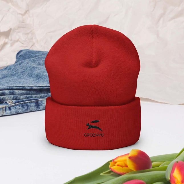 Cuffed Beanie in red color displayed on a flat surface with flowers and denim in the background.