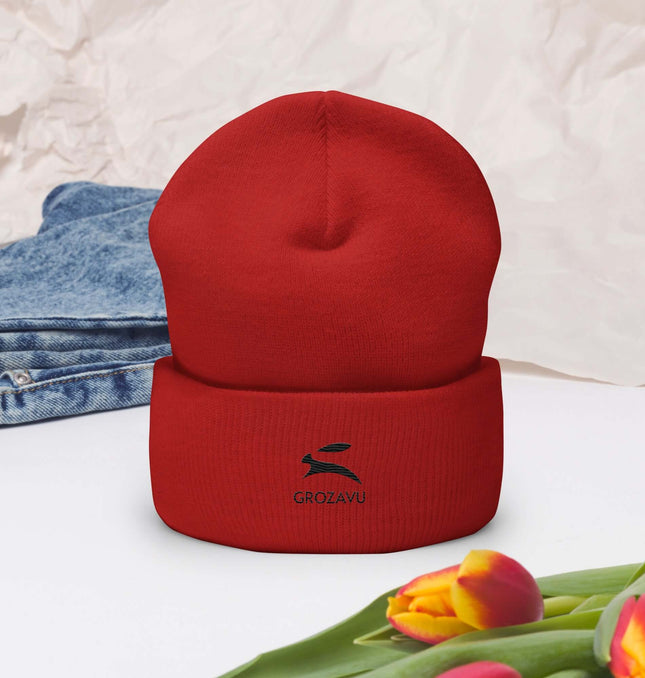 Cuffed Beanie in red color displayed on a flat surface with flowers and denim in the background.