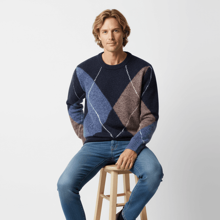 Man wearing a Diamond Pattern Knit Sweater with blue and brown diamond patterns, sitting on a stool.