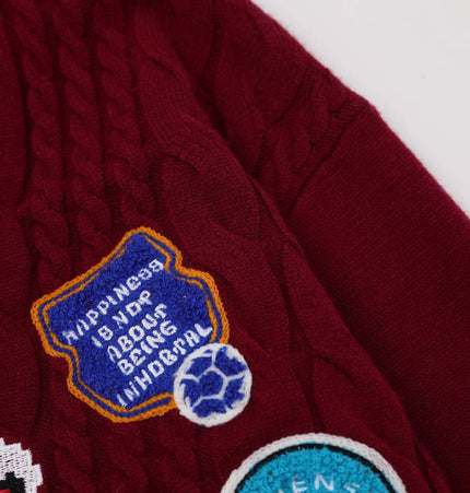 Close-up of the Grozavu Embroidered Cable Knit VNeck Sweater showcasing embroidered patches on a maroon fabric.
