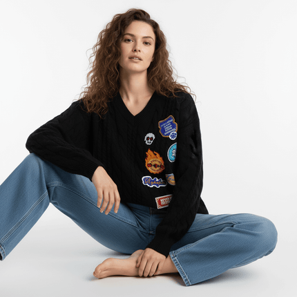 Embroidered Cable Knit VNeck Sweater worn by a model sitting, showcasing its unique patches and relaxed fit.