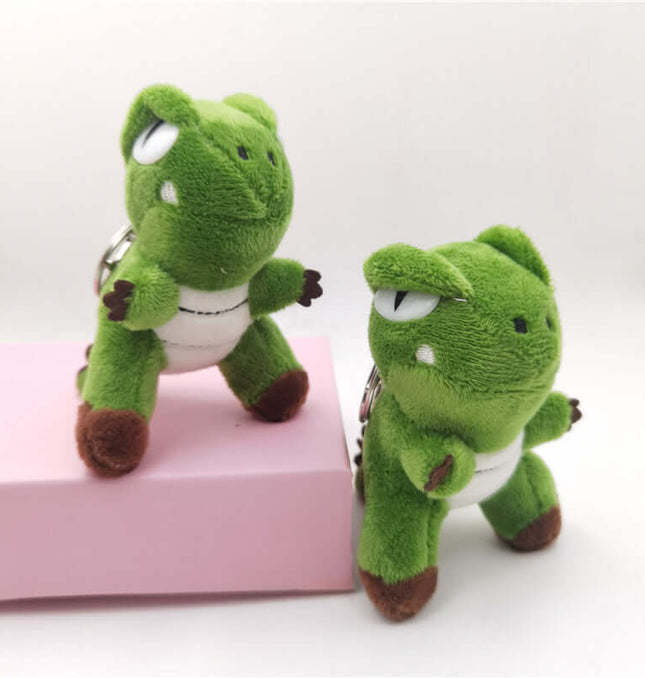 Green Dinosaur Plush Keychain set showing two cute green dinosaur plush figures on a pink background.