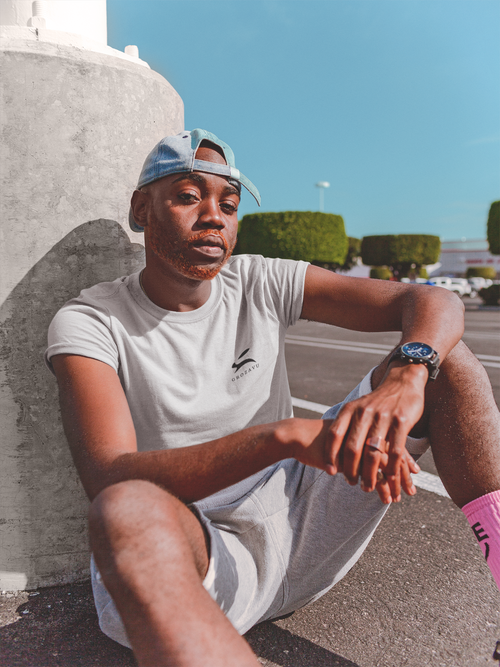 Male model seated outdoors in light grey Grozavu logo T-shirt — casual premium-cotton streetwear lifestyle