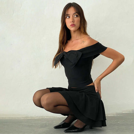 Slim Fit One-Shoulder Bow Top worn by a woman posing elegantly in a black skirt and heels.