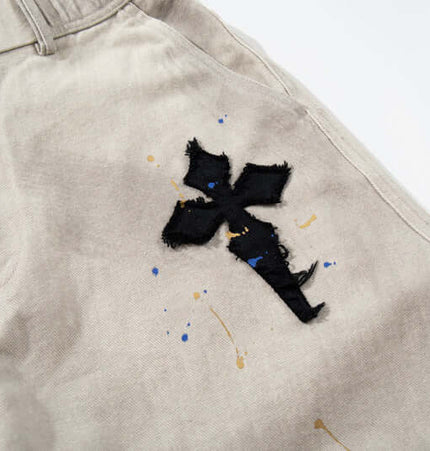 Close-up of Straight Leg Patchwork Denim Jeans with cross patch embroidery and color splatter detailing.